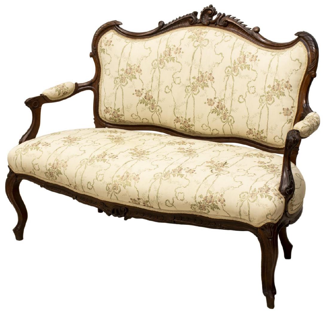 LOUIS XV STYLE UPHOLSTERED PARLOR SETTEE SOFA: Louis XV style parlor settee, having walnut frame, with carved center crest, over upholstered back, armrests, and seat, in floral patterned textile, rising on cabriole legs, approx 38.25"h, 50.25"w, 2