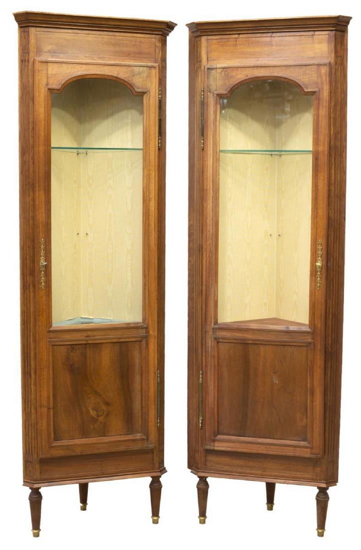 (2) FRENCH LOUIS XVI STYLE WALNUT CORNER CABINETS: (lot of 2) French Louis XVI style walnut corner cabinets, 20th c., having cornice top, over partially glazed door on exterior hinges, opening to interior with silk moire backing and shelves, rising on