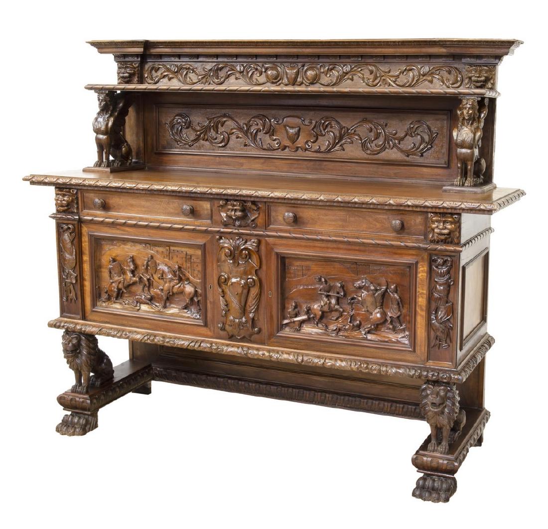 ITALIAN RENAISSANCE REVIVAL CARVED WALNUT BUFFET: Italian Renaissance Revival walnut buffet/ server, early 20th c., carved with running ornamentation, grotesques, heraldic crests and battle scenes, upper shelf supported by standards in form of sphinx
