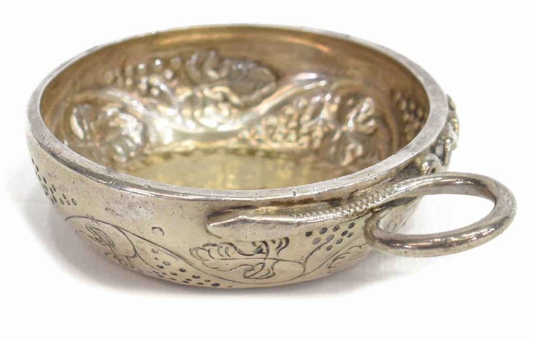 FRENCH 800 SILVER TASTEVIN SERPENT-FORM HANDLE, 18th C.: French 800 silver tastevin (wine tasting cup), 18th C., having serpent-form handle, body with chased grapevine motif, approx 1"h, 4.25"w, 4.46ozt total Start Price: $150.00