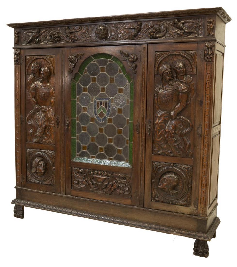 SPANISH RENAISSANCE REVIVAL STAINED GLASS BOOKCASE: Spanish Renaissance Revival carved walnut and stained glass bookcase, 19th c, having running ornamentation to cornice, ornately carved throughout with figural busts, grotesques and cherubs, center doo