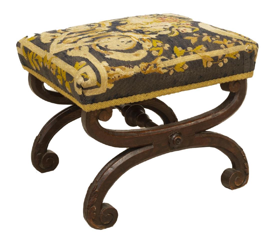 NEOCLASSICAL NEEDLEPOINT CURULE FOOTSTOOL: Continental neoclassical footstool, late 19th c., worn needlepoint upholstered seat, on oak curule base with scrolled foliate feet, joined by turned center stretcher, approx 17"h, 19.5"w, 15.5"d Start