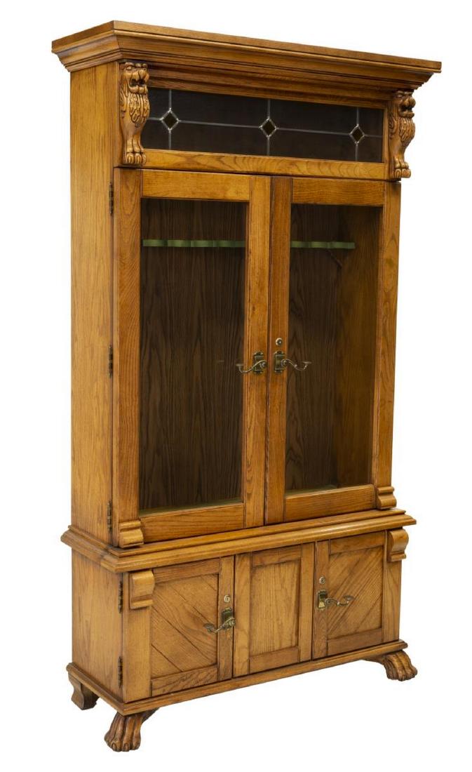 AMERICAN CARVED OAK GUN CABINET, 20TH C.: American oak gun cabinet, 20th c., the stepped cornice over a stained and leaded panel flanked by carved griffins, glazed cabinet doors opening to gun storage, above two small cabinet doors, rising on