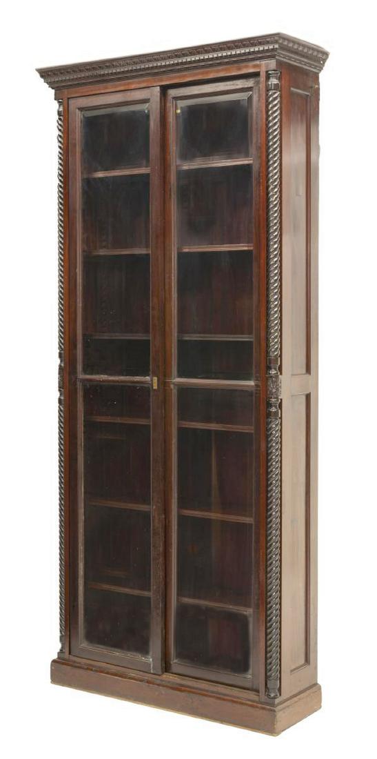 MAHOGANY SLIDING GLASS DOOR BOOKCASE: Sliding glass door bookcase, 20th c., having a stepped cornice accented by running ornamentation above sliding doors set with beveled glass panes, flanked by spiral turned standards with floral carvin