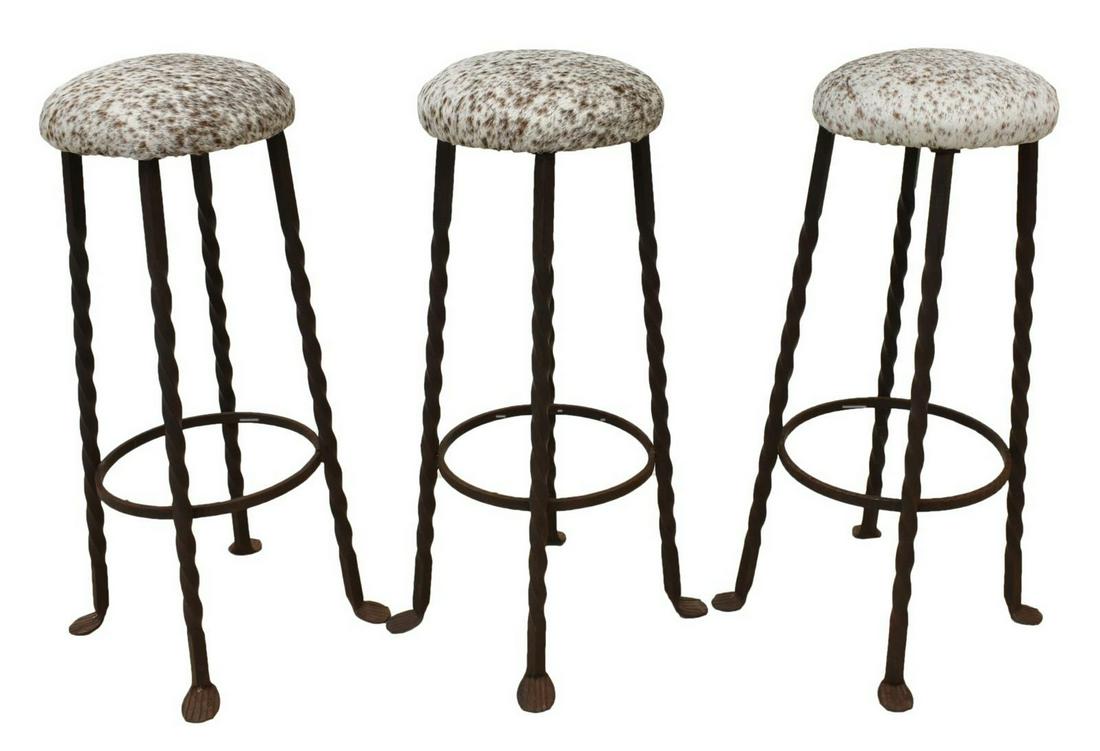 (3) HAND-FORGED IRON BAR STOOLS COWHIDE SEATS: (lot of 3) Hand-forged iron bar stools, late 20th c., with spotted cowhide covered seats, stretcher-joined spiral supports, ending in pad feet, approx 31"h, 11.75"diam Start Price: $80.00