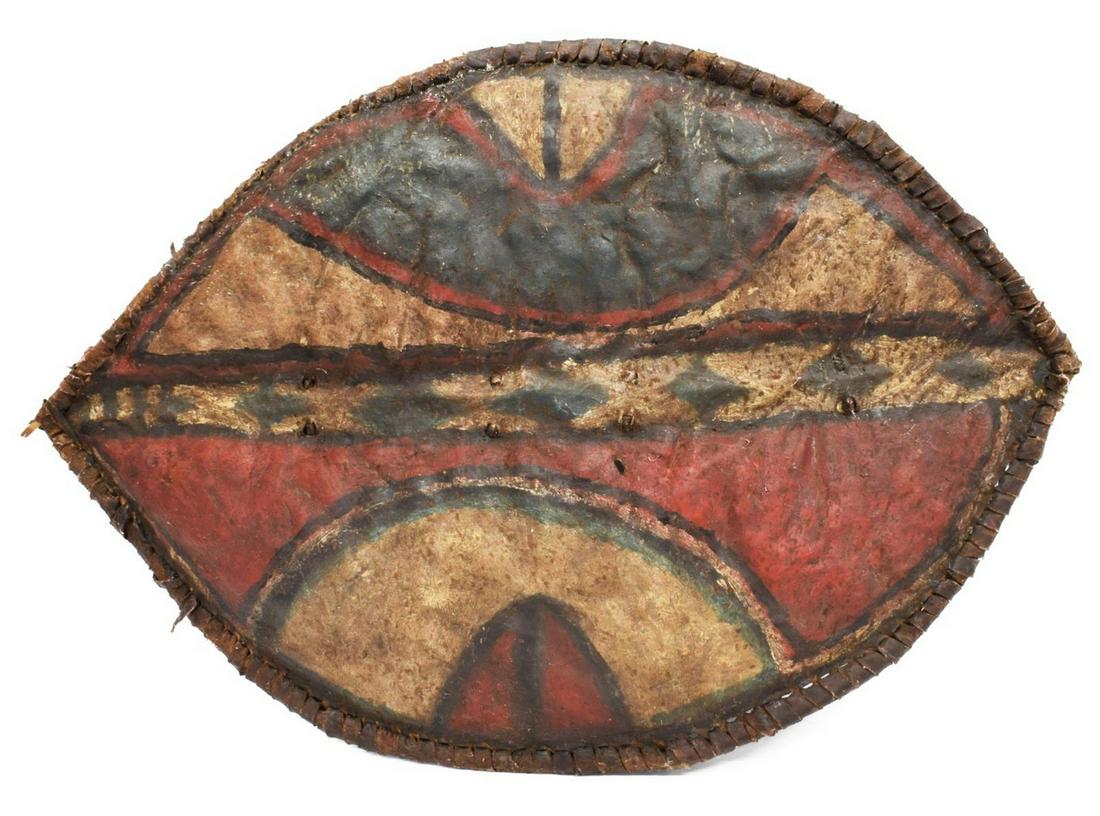 AFRICAN TRIBAL KENYAN MAASAI ANIMAL HIDE SHIELD: African tribal Kenyan Maasai animal hide warrior shield, of oval form stretched and sewn over wood frame, with affixed handle at back, geometric design in natural pigments including red, black and blu
