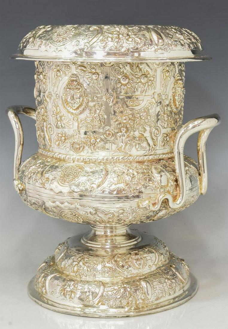 NEOCLASSICAL SILVERPLATE URN-FORM WINE COOLER: Neoclassical silverplate urn-form wine cooler, with removable insert, serpent handles, body profuse with relief decoration including grotesque masks, fruit, birds, figures, and animals, raised on circ