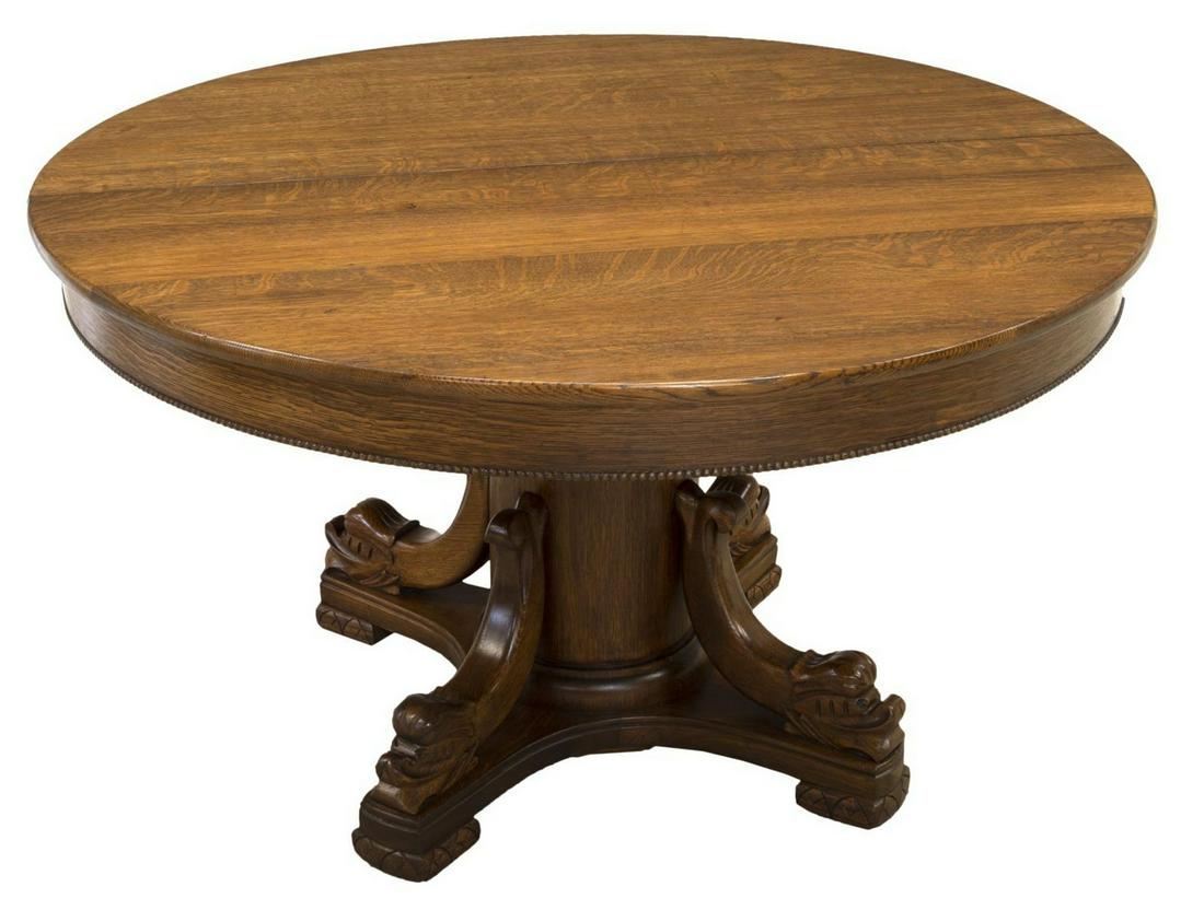 AMERICAN OAK SPLIT PEDESTAL DOLPHIN DINING TABLE: American oak extension split-pedestal dining table, c. 1900, the round top over a beaded skirt, rising on a cylindrical pedestal, four stylized dolphins on the raised base, not accompanied by leaves,