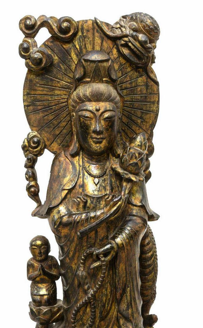 LARGE CHINESE PARCEL GILT CARVED QUAN YIN FIGURE: Large Chinese parcel gilt carved wood sculpture of Quan Yin and child attendant, heavily carved, deity shown wearing long robe, celestial scarf with hair elaborately tied and veiled, surmounted by dra