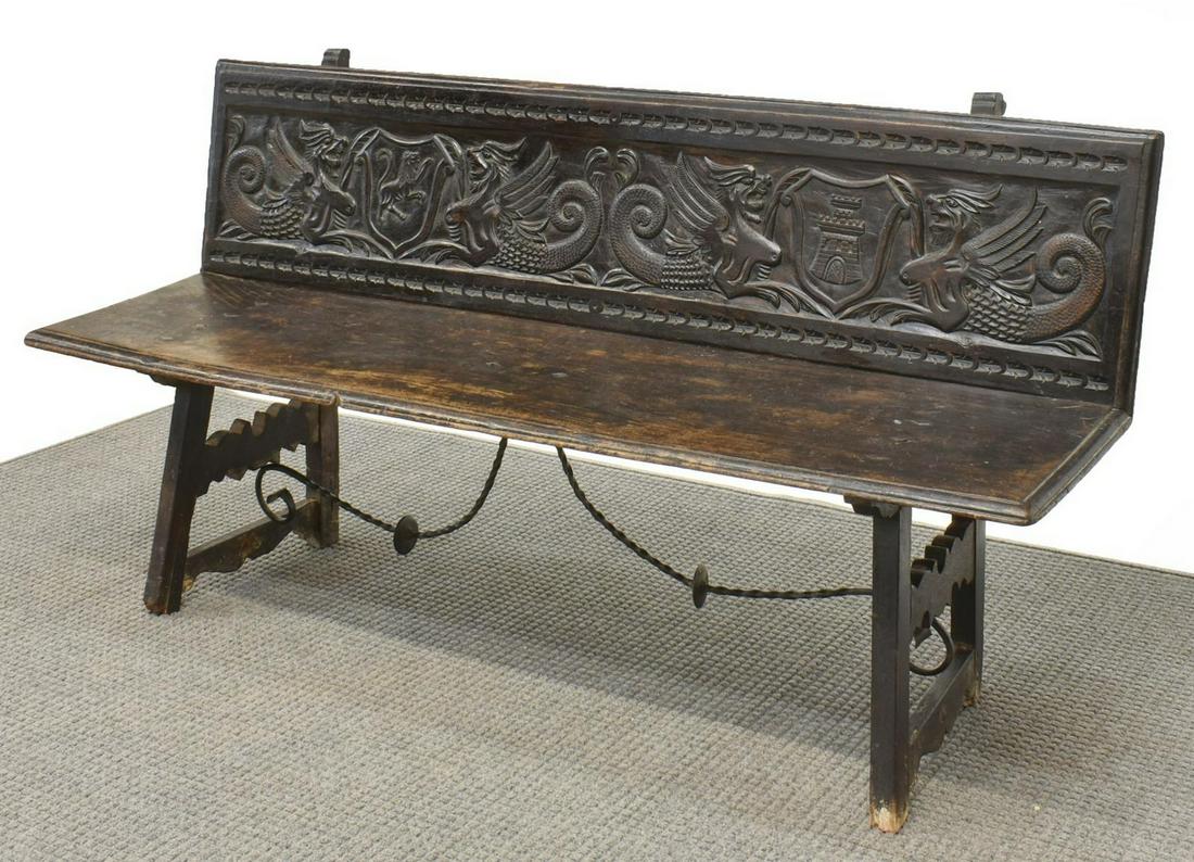 SPANISH RENAISSANCE REVIVAL CARVED BENCH, 66"L: Spanish Renaissance Revival bench, 19th c., plank back and seat, back carved with grotesques centering heraldic shields, one with lion rampant, one with tower, rising on trestle base joined by scrolle