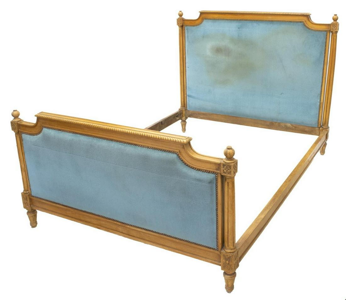 FRENCH LOUIS XVI STYLE UPHOLSTERED BED: French Louis XVI style bed, early 20th c., having blue velveteen upholstery, accented by brass tacking and floral carving, the headboard and footboard each flanked by carved finial topped round fluted