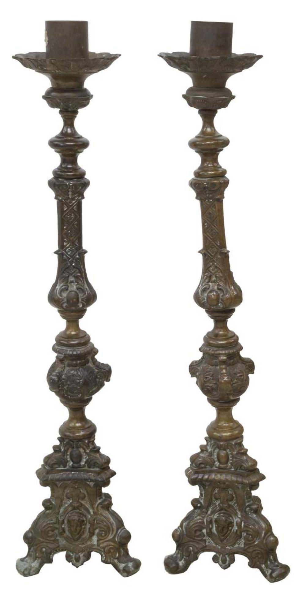(PR) LARGE MEXICO PATINATED BRONZE ALTAR LIGHTS: (pair) Patinated bronze altar lights, Mexico, having single candle cup atop a shaped standard with geometric and foliate elements, rising on tripartite base accented by cherub mask motifs, scrollwork 