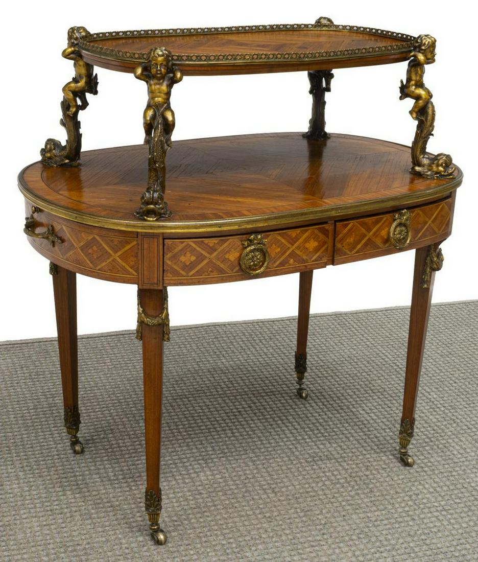 FRENCH LOUIS XVI STYLE TWO-TIER DESSERT TABLE: French ormolu and marquetry accented two-tier dessert table, late 19th c., the upper tier rising on figural and dolphin supports above the lower oval tier over faux drawer fronts at three sides, pull 