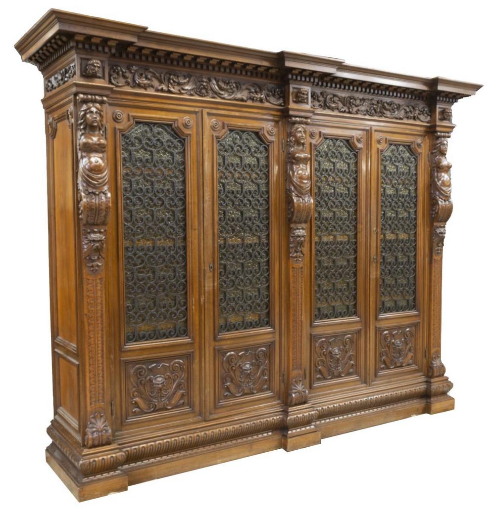 RENAISSANCE REVIVAL FIGURAL CARVED WALNUT BOOKCASE: Italian Renaissance Revival walnut bookcase, early 20th c., molded cornice over carved frieze with projecting masks, scrolling foliates, female figural pilasters, four doors with textured glass insets