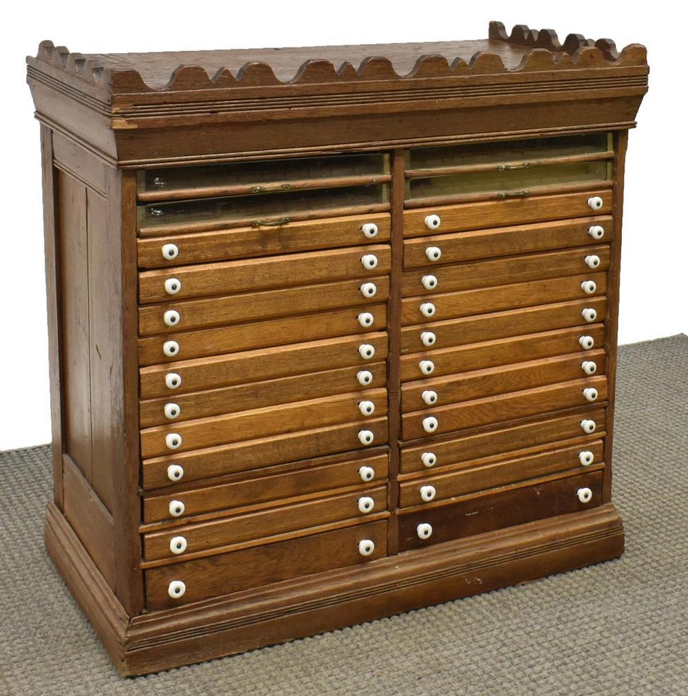 AMERICAN GENERAL STORE OAK SPOOL CABINET: American oak spool cabinet, c.1900s, four glazed drawers, over twenty-two drawers with porcelain pulls, rising on a plinth base, splits to side panels, losses to crown molding, 36.5"h, 36.5"w, 19"d St