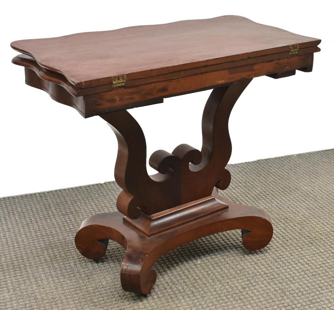 AMERICAN EMPIRE MAHOGANY FLIP TOP GAMES TABLE: American Empire flame mahogany games table, blind stamped F. Fabian, 19th c., shaped hinged top, over lyre harp support with floral and scroll carving, platform base with scrolled legs, on casters, to