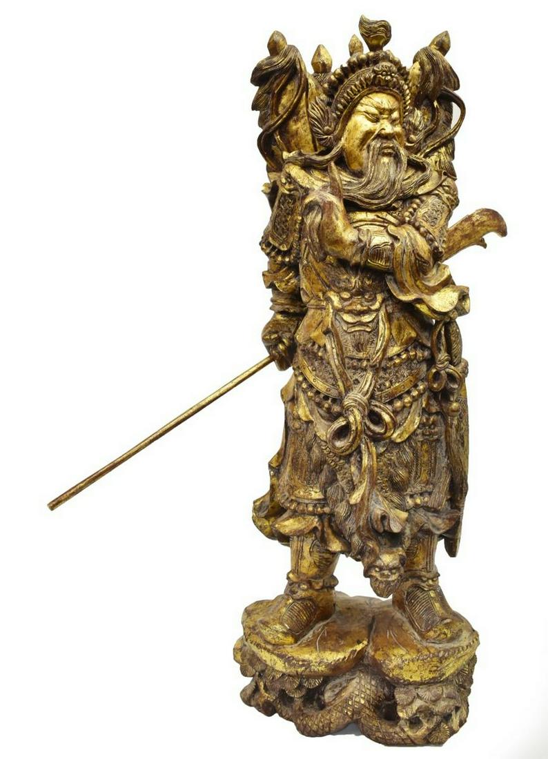 CHINESE CARVED & GILT GUAN YU WARRIOR FIGURE: Chinese carved and gilt figure of a warrior, likely Guan Yu, with flags at his back, posed holding a spear, standing on a rocky base with pine branches, approx 35.25"h, 53lbs Start Price: $100.00