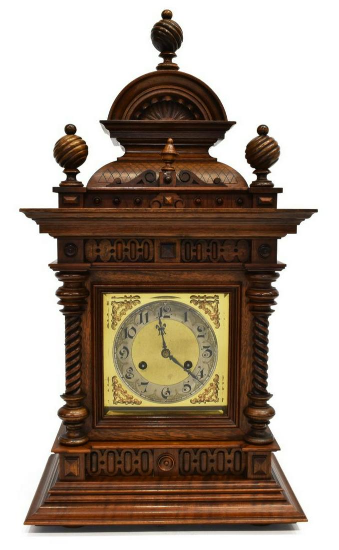 GERMAN JUNGANS WALNUT BRACKET MANTEL CLOCK: German Jungans bracket mantel clock, in walnut case, having an elaborate arched cornice with turned finials, scalloped and quilted carving, over face with black Arabic numerals, gilt scrolling accents