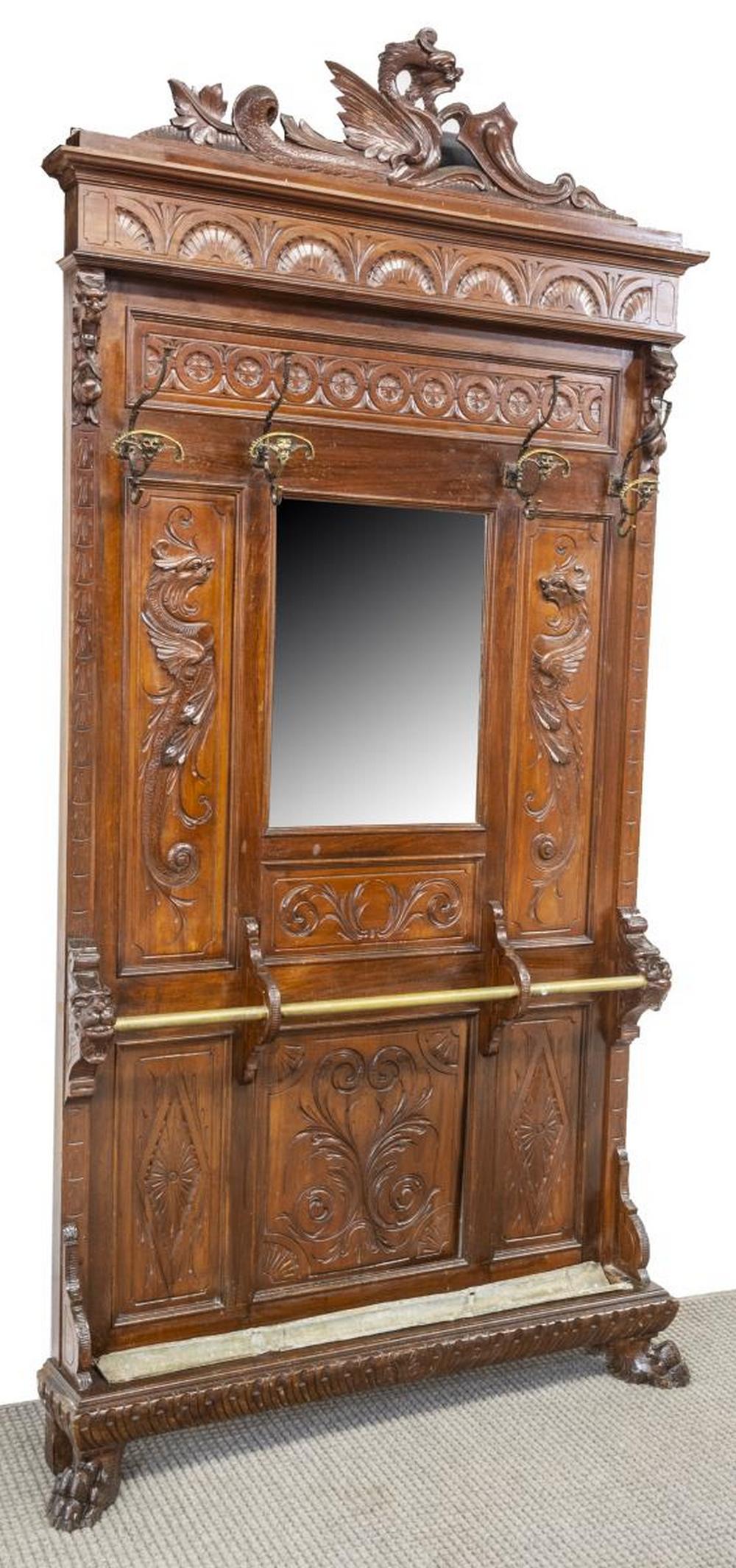 ITALIAN RENAISSANCE REVIVAL CARVED HALL TREE: Italian Renaissance Revival hall tree, 19th c., having a scrolled dragon crest, over foliate carved back, four scrolled coat hooks, centered beveled mirror, flanked by dragons, over umbrella rack and 