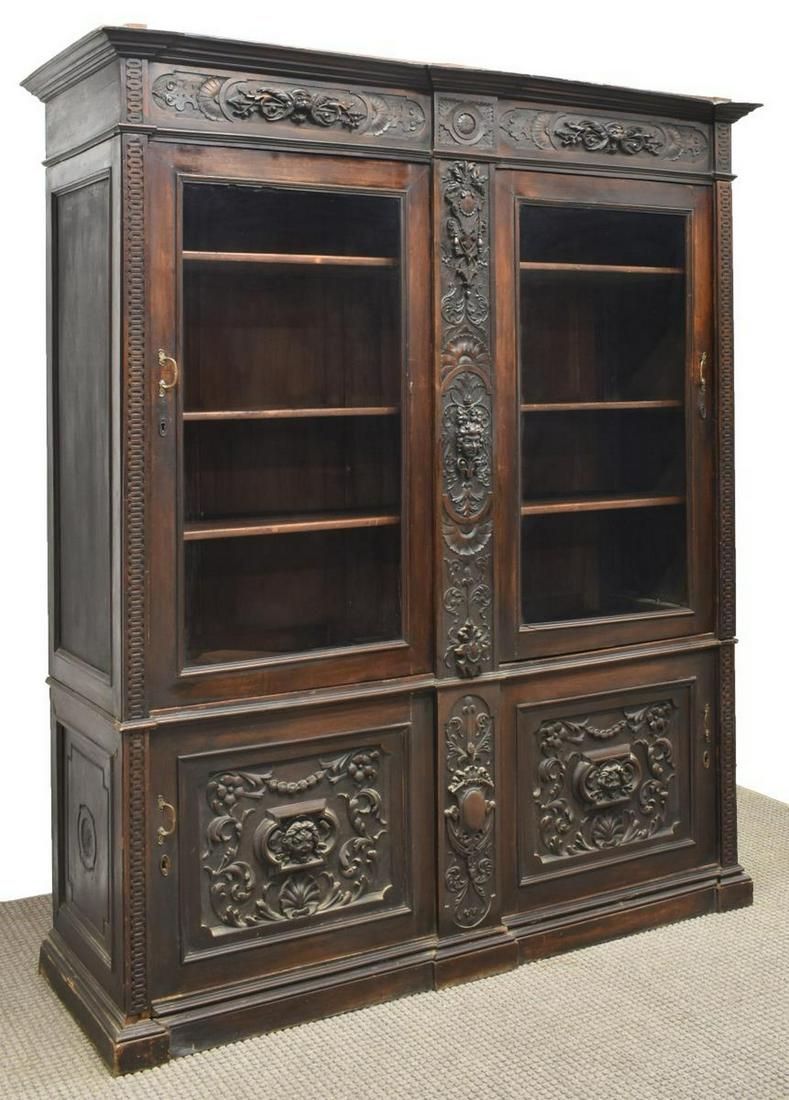 RENAISSANCE REVIVAL FIGURAL CARVED BOOKCASE: Renaissance Revival figural carved bookcase / display cabinet, in dark finish, having molded cornice, over extensive carving of figural masks, scallops, shields, and scrolling foliates, fitted with do