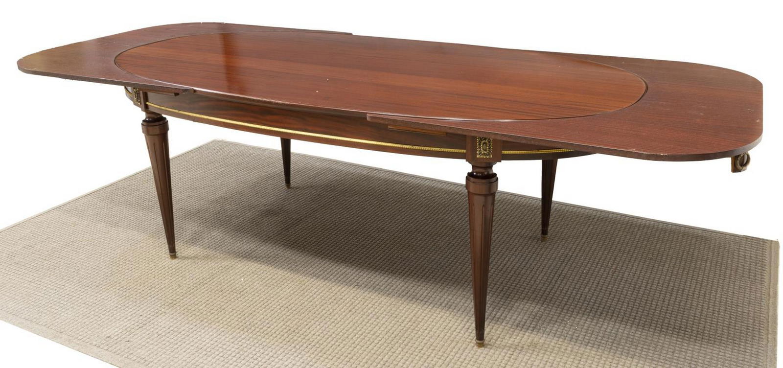 LOUIS XVI STYLE MAHOGANY EXTENSION DINING TABLE: French Louis XVI style mahogany dining table, 20th c., oval tabletop with foliate parcel gilt floral accents, slides to support leaves at either end, with gilt wreath-form hanging pulls, accompanied b