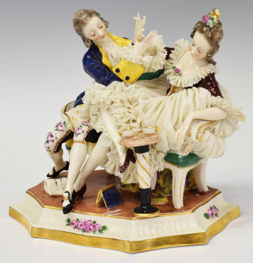 DRESDEN LACE PORCELAIN COUPLE FIGURE GROUP: Continental porcelain figure group, possibly Capodimonte or Volkstedt, early 20th c., a beauty in Dresden lace skirt, accented with applied flowers, seated on a parcel gilt sofa with gentleman suitor,