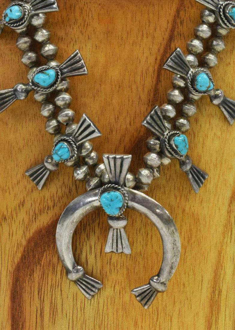 NATIVE AMERICAN TURQUOISE SQUASH BLOSSOM NECKLACE: Native American silver (content unknown) squash blossom necklace, bench bead strand, twelve blossoms, central naja, each with a bezel-set turquoise cabochon, approx 25.5"l, naja: approx 2 5/8"h, 2 1/8