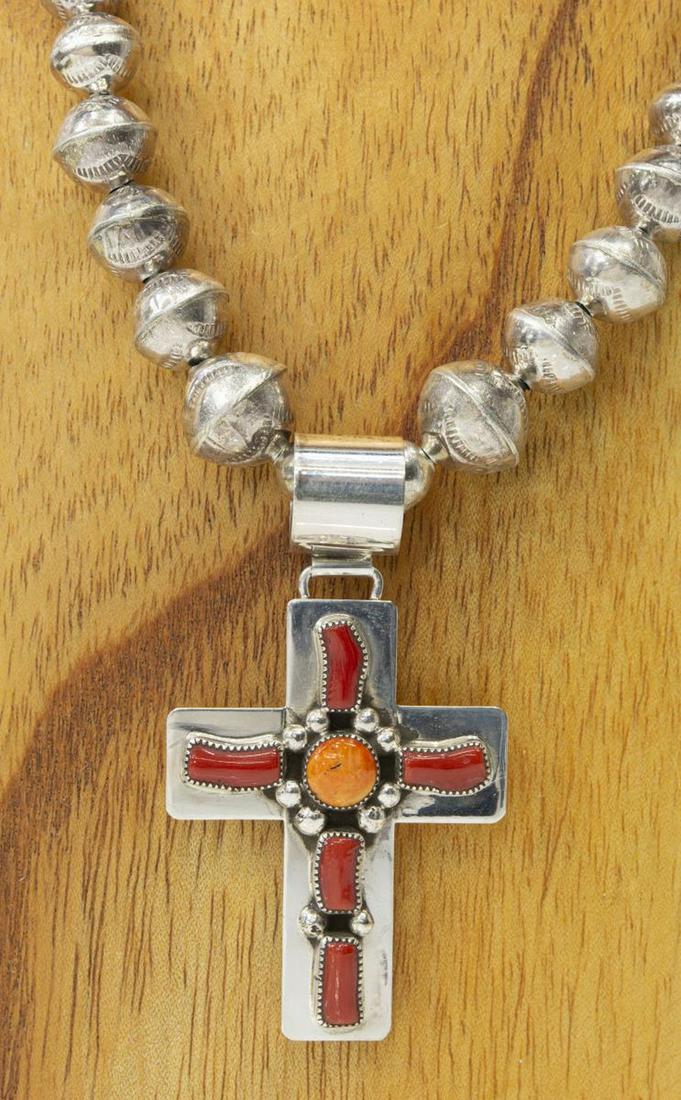 KENNETH JONES NAVAJO RED CORAL CROSS PENDANT: Native American sterling silver necklace, hallmarked J with crossed arrows (Kenneth Jones, Navajo, 20th c.), cross-form pendant with bezel-set red coral cabochons, on graduated bench bead strand, appr