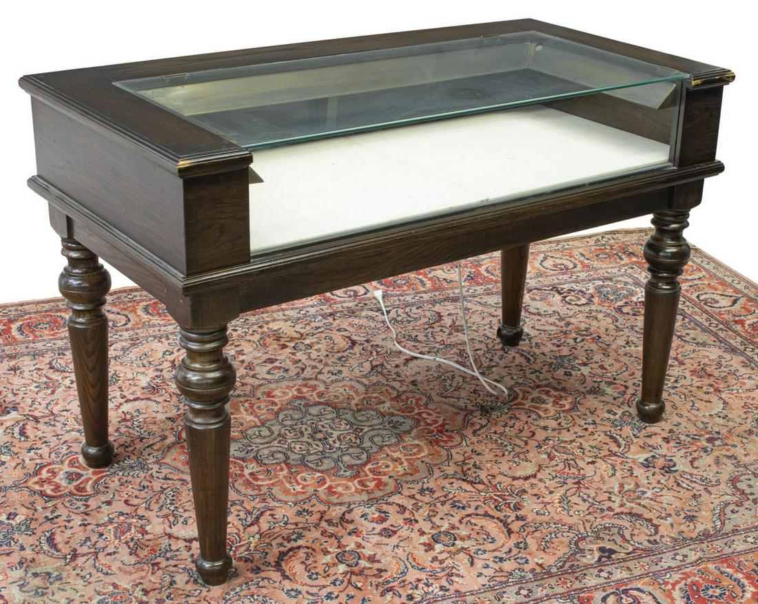 OAK FRAMED RETAIL STORE DISPLAY CASE TABLE: Retail display case, late 20th c., oak frame with glazed top and front panels, linen interior, back with dual sliding doors, interior lighting, rising on turned legs, approx 32"h, 49"w, 25"d Start Pri