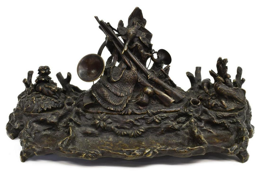 PATINATED BRONZE HUNT DOUBLE INKWELL DESK STAND: Patinated bronze encrier desk stand, late 19th c., with motifs drawn from the hunt, center compartment lid with rifles, horns, and powder flask, flanked by inkwells, one lid with hare, one lid with ph