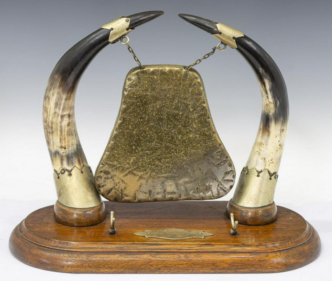BURMESE HORN & BRASS TABLE GONG: Table gong, the shaped brass gong suspended from a pair of horns, stamped Burmese, mounted on an oval wood base with central cartouche, approx 12.5"h, 17"w, 8"d, 7lbs Start Price: $50.00
