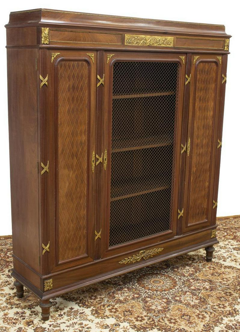 FRENCH EMPIRE STYLE MAHOGANY BOOKCASE: French Empire style gilt metal mounted mahogany bookcase, early 20th c., cavetto-molded cornice above frieze with gilt metal plaque depicting winged putti, reeded verticals, three doors, center with m