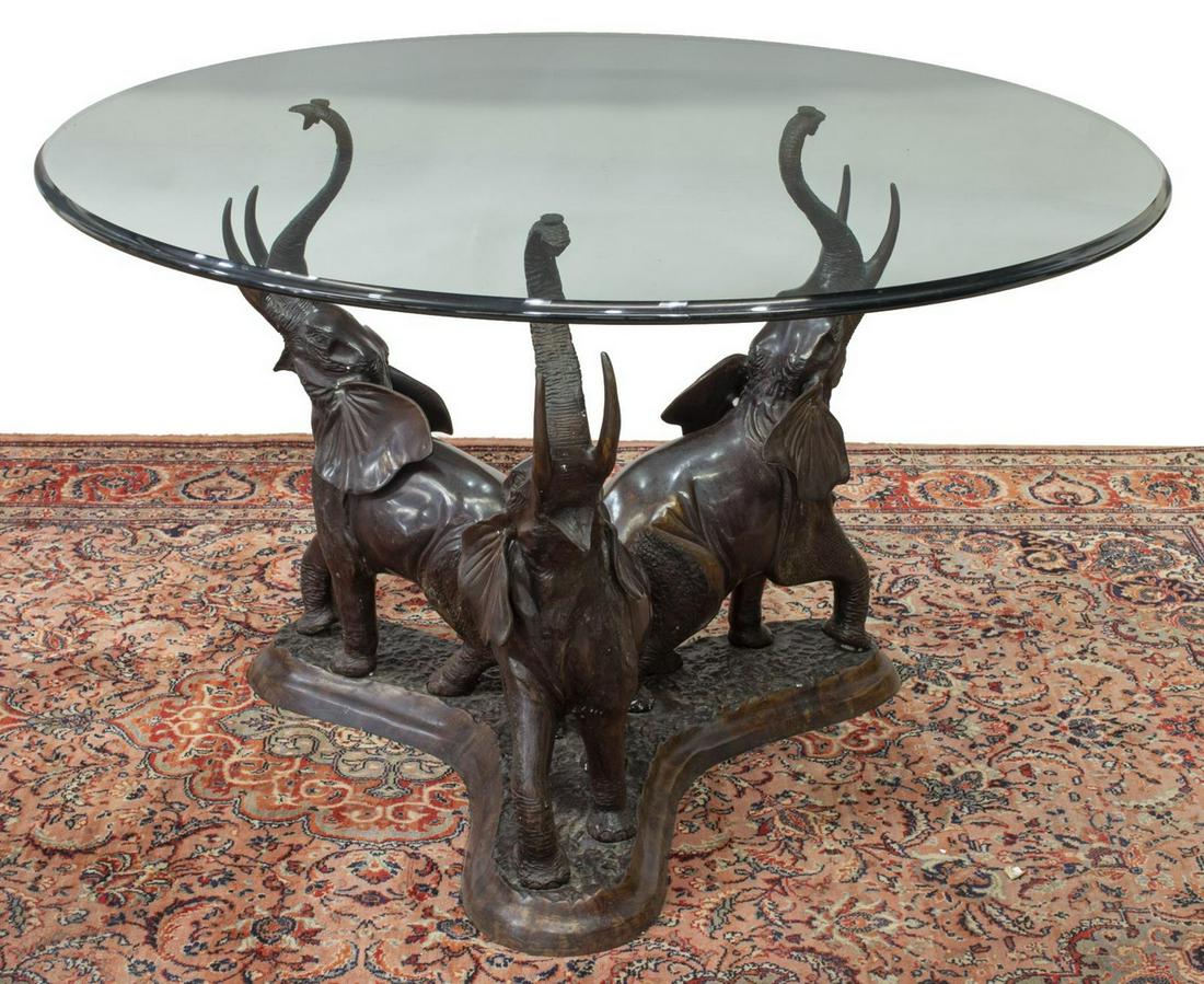 BRONZE ELEPHANT 47.5"DIAM GLASS-TOP TABLE: Bronze elephant center table, 20th c., circular glass top with beveled edge, over tripartite figural support of elephants, each with raised trunk, mouth ajar, on conforming base, approx 29.75"h, 47.5"