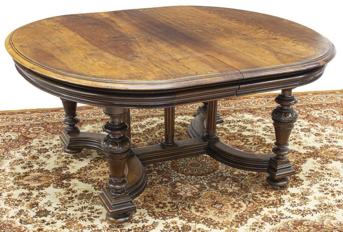 FRENCH HENRI II STYLE WALNUT EXTENSION TABLE: French Henri II style walnut dining table, 19th c., oval tabletop with molded edges, architectural columnar supports joining turned legs, with foliate carved accents, rising on bun feet, on casters, n