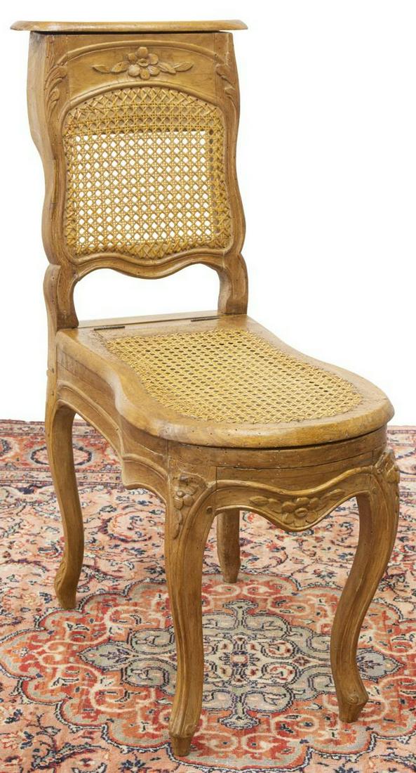 FRENCH LOUIS XV STYLE CANE COMMODE CHAIR: French Louis XV style commode chair, 19th c., hinged compartment with divided interior in top rail, floral carved frame, cane back and hinged seat, faience insert with blue glazed floral decoration, r