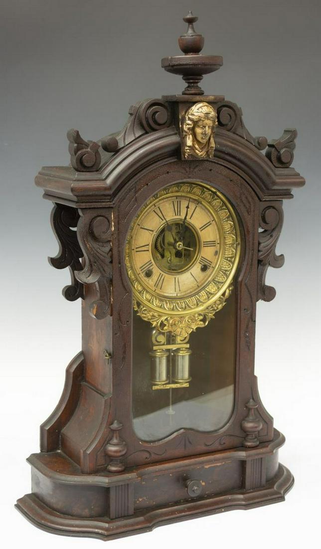 AMERICAN ANSONIA 'MONARCH' CARVED SHELF CLOCK: American Ansonia "Monarch" mantel shelf clock, late 19th/ early 20thc., in dark finish, having time and strike movement, turned finial, parcel-gilt figural head, over case with scrolled carvings, hing