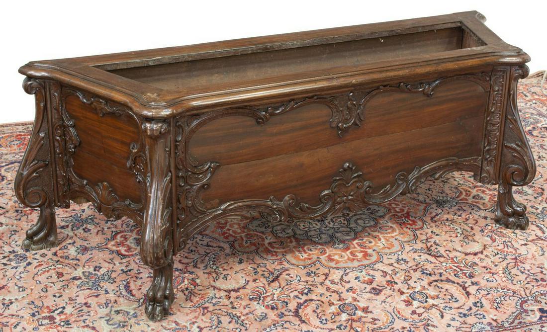 ITALIAN CARVED JARDINIERE PLANTER: Italian mahogany jardiniere, early 20th c., shaped case, with carved foliate and scrollwork motifs, rising on paw feet, missing foliate accents to front right, approx 20"h, 58"w, 19.5"d Start Price: $