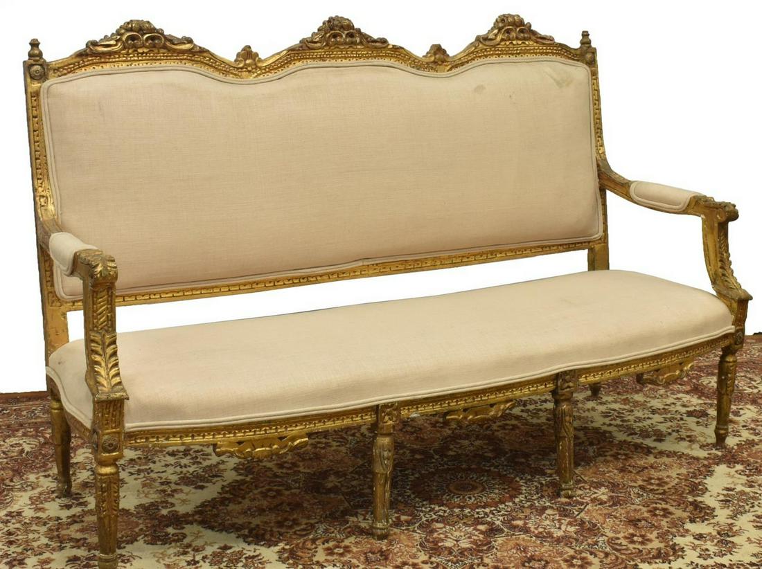 FRENCH LOUIS XVI STYLE CARVED GILTWOOD SALON SOFA: French Louis XVI style giltwood salon sofa, having cream upholstery to back, seat, and arms, with carved floral crests to upper rail, foliate accents throughout, on fluted tapered legs, approx 43"h, 6