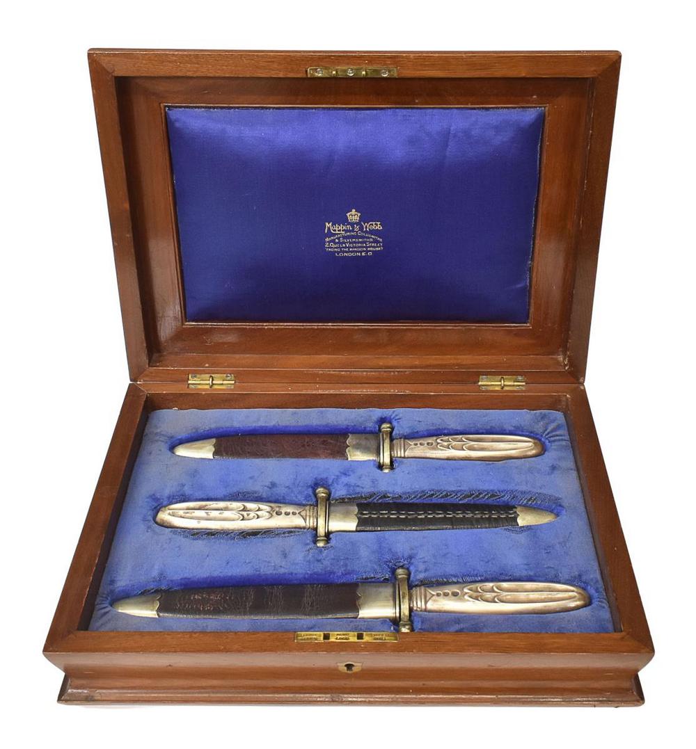 (3) ENGLISH MAPPIN & WEBB CASED DAGGER SET: (lot of 3) Mappin & Webb cased dagger set, United Kingdom, housed in figured elmwood case, with central shield-form brass cartouche, each knife in leather sheath, with German silver to tip and throat,