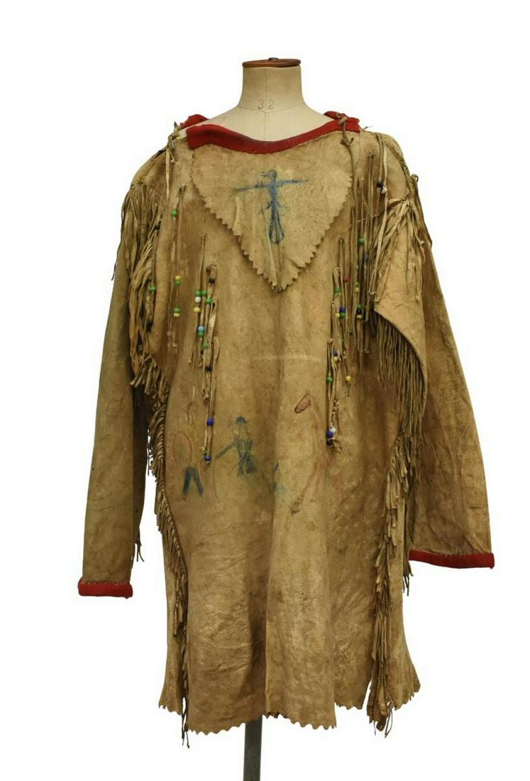 NATIVE AMERICAN PICTORIAL HIDE SHIRT, C.1920-1940: Native American hide shirt, c.1920-1940, red wool collar and sleeve binding, fringe with large glass beads, blue pigment bird at bib, figural scene with two Native American warriors, one on horseback,