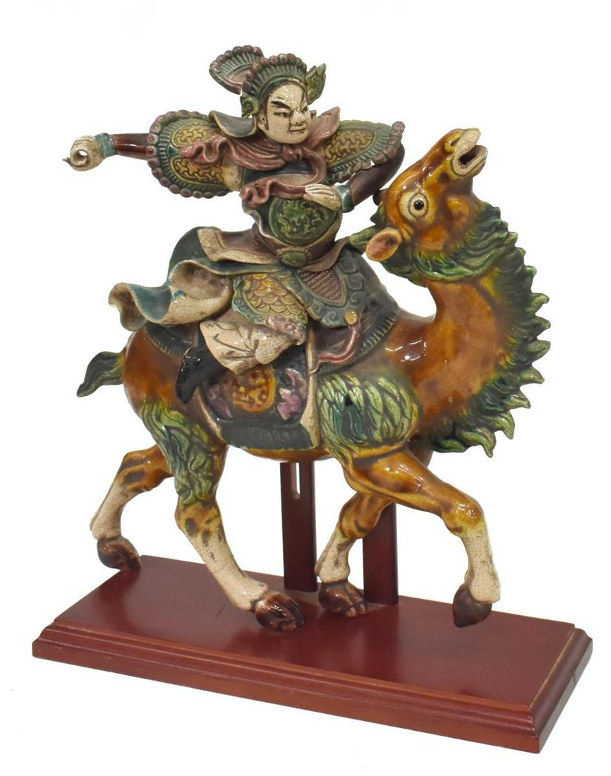CHINESE GLAZED POTTERY FIGURAL ROOF TILE: Chinese glazed pottery figural roof tile, warrior astride a camel, impressed mark, mounted to wooden display stand, losses to helmet and shoulder armor, overall: approx 15"h, 13.5"w, 5"d, 7.5lbs Start