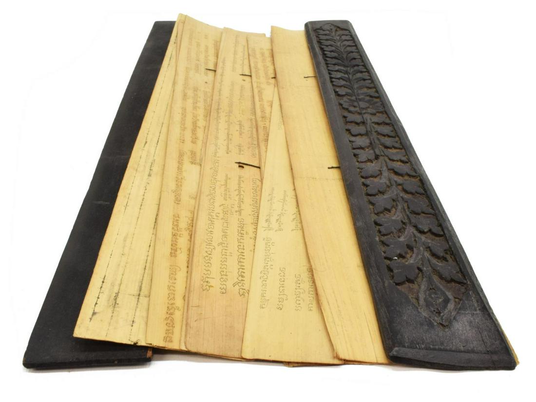 TIBETAN BUDDHIST SUTRA, CARVED COVER, PALM LEAVES: Tibetan Buddhist sutra, within black foliate-carved wood covers, ten palm leaf pages, most inscribed on both sides and secured to the covers by light, loose black string, covers: approx 1.5"h, 23.5"w,