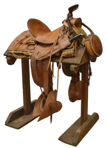IMPRESSIVE WESTERN SADDLE IN BASKETWEAVE PATTERN: Western saddle, light brown leather highly tooled in basket weave pattern with concho accents, approx 15.75" seat, complete with stirrup tapaderos, cased Joaquin machete, quirt, metal canteen in match