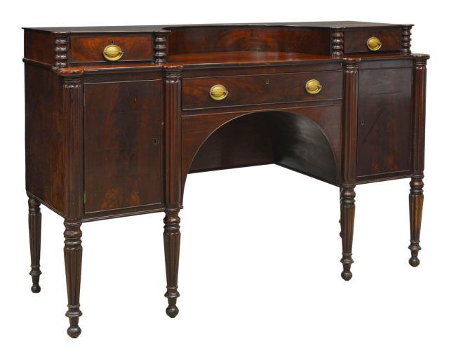 AMERICAN SHERATON STYLE MAHOGANY SIDEBOARD: American Sheraton style mahogany sideboard, 19th c., concave superstructure with two drawers, over central drawer, side cabinets opening to shelves, arcaded front, reeded corner posts continuing to ta