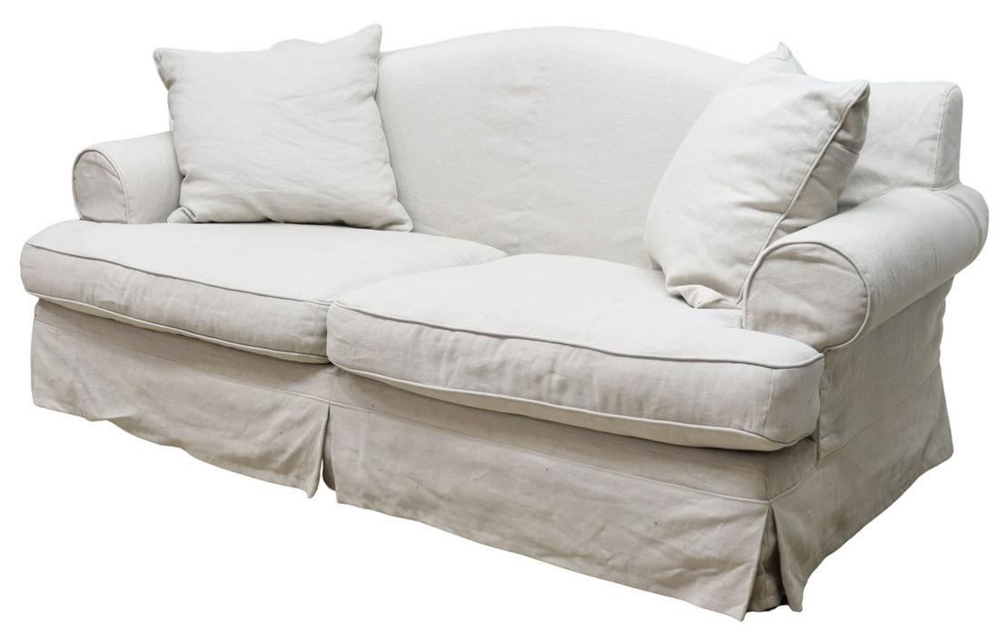 NATURAL LINEN SLIPCOVERED CAMELBACK SOFA: Contemporary linen slipcovered camelback sofa, late 20th c., with rolled arms, two loose seat cushions, skirted base concealing wood block legs, accompanied by (two) throw pillows, some spotting to up