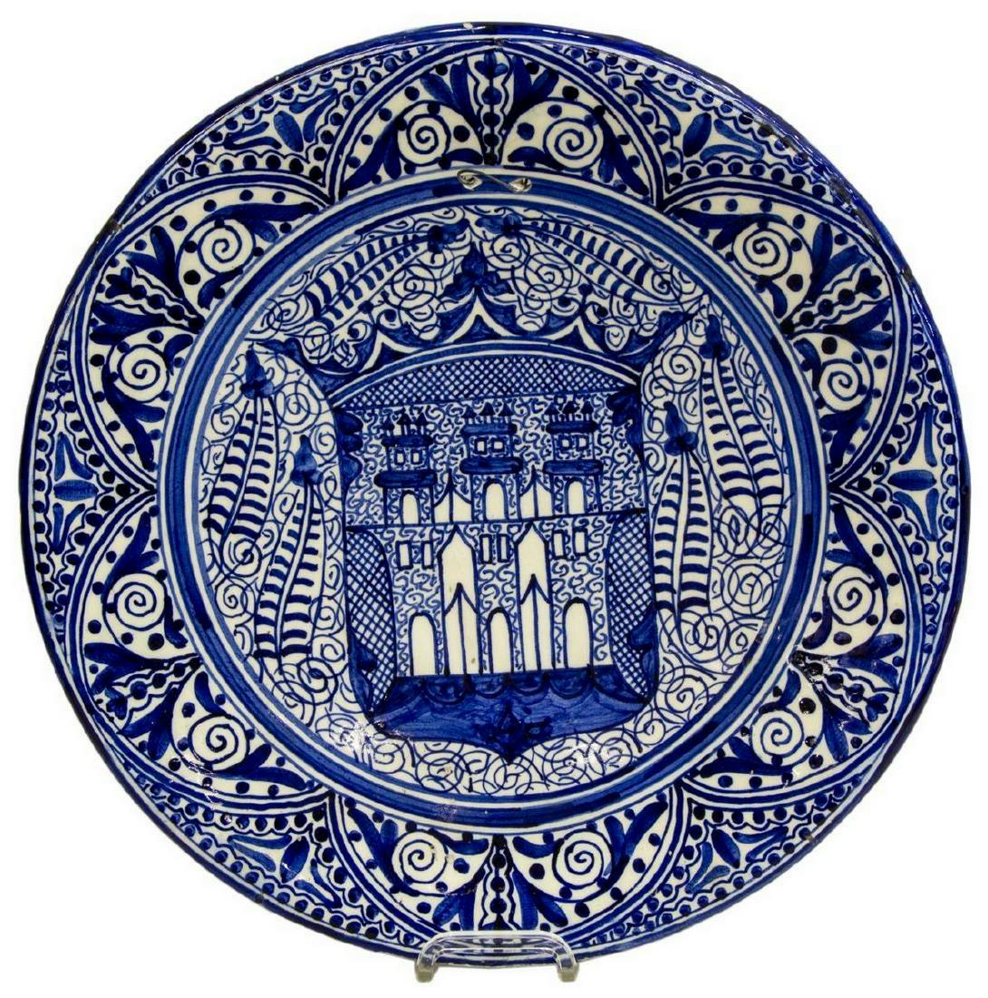 LARGE SPANISH MAJOLICA EARTHENWARE CHARGER: Large Spanish majolica earthenware charger, 20th c., blue glaze on white ground, having scrolling floral and foliate motifs, heraldic shield with castles emblazoned to center, pierced for hanging, som