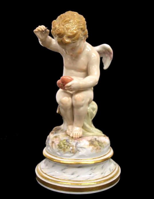 MEISSEN PORCELAIN CUPID FIGURE SEWING HEART: Meissen porcelain figure, late 19th/early 20th c., modeled as a winged cupid mending a broken heart, raised on a marbelized base with gilt borders, blue crossed swords mark underglaze, incised L101, s
