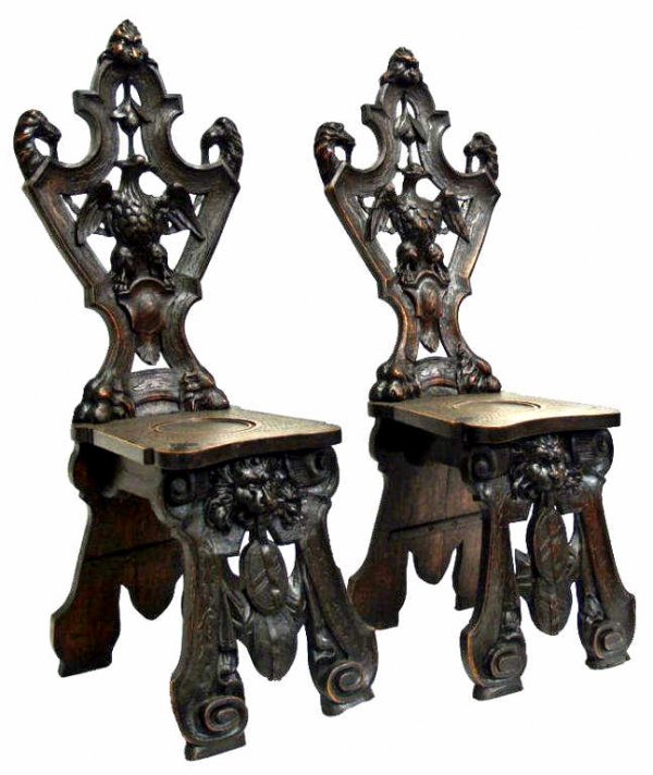 ANTIQUE BLACK FOREST EAGLE CARVED HALL CHAIRS: Pair of Swiss Black Forest carved walnut hall chairs, late 19th c., the pierced back of each carved with animal heads in profile and centering a full bodied eagle, the base equally as elaborate featur