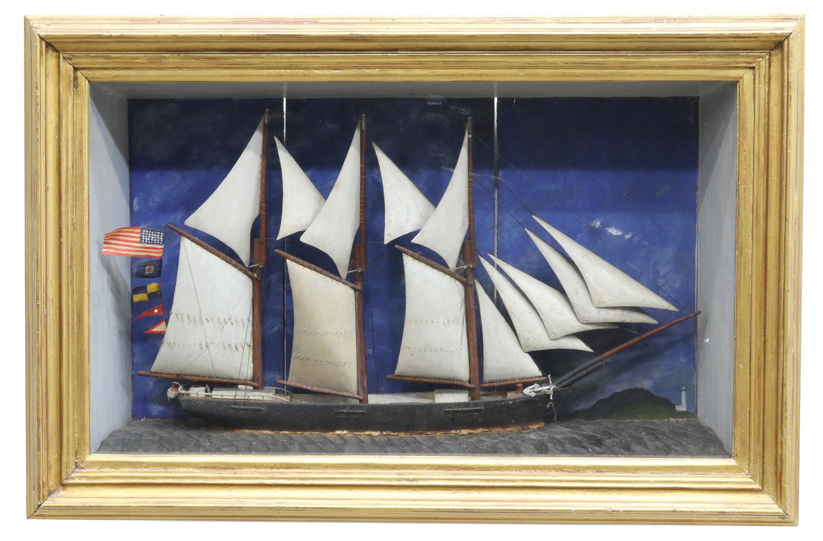 AMERICAN FOLK ART FRAMED SHIP DIORAMA, 19TH C.: American Folk Art framed ship diorama, New England, 19th c., depicting an American three-masted schooner, displayed in glazed giltwood frame, against painted paneled back, initialed J in lower right c