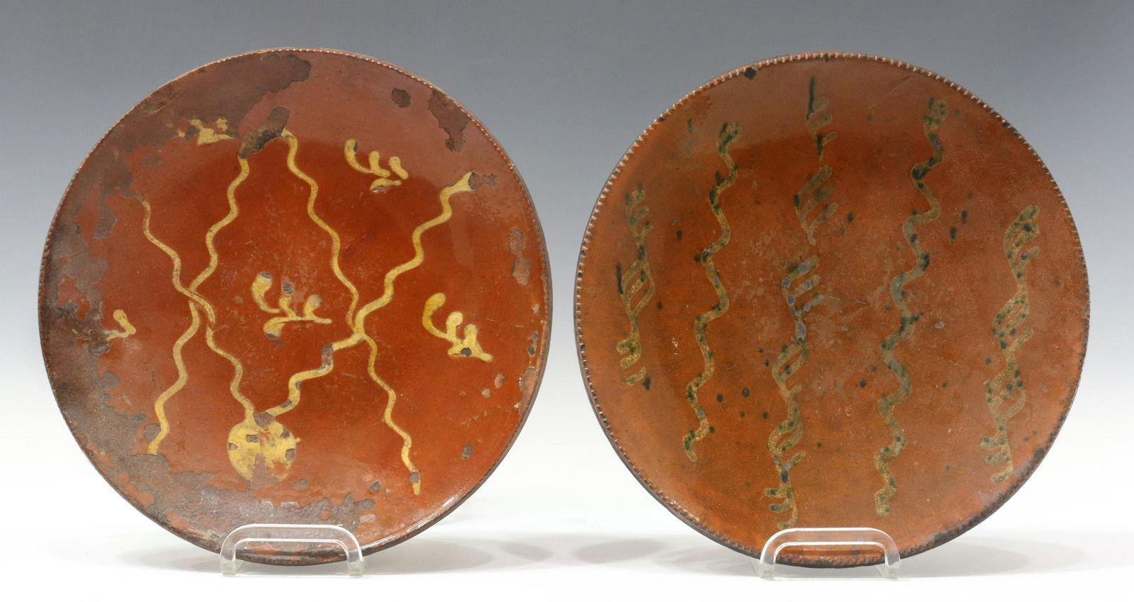 (2) AMERICAN SLIP-DECORATED REDWARE POTTERY PLATES: (lot of 2) American slip-decorated redware pottery plates, New England, 19th c., having a coggled rim, encircling linear yellow slip cup designs, unglazed bottom, expected rim and glaze chips, crazing
